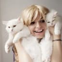 A blonde woman affectionately holding two white cats next to her face as if she were cuddling them!