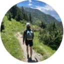 girl with hat and backpack walking along a path into a forest